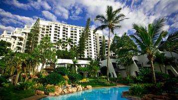 A hotel with a swimming pool surrounded by lush greenery and palm trees.