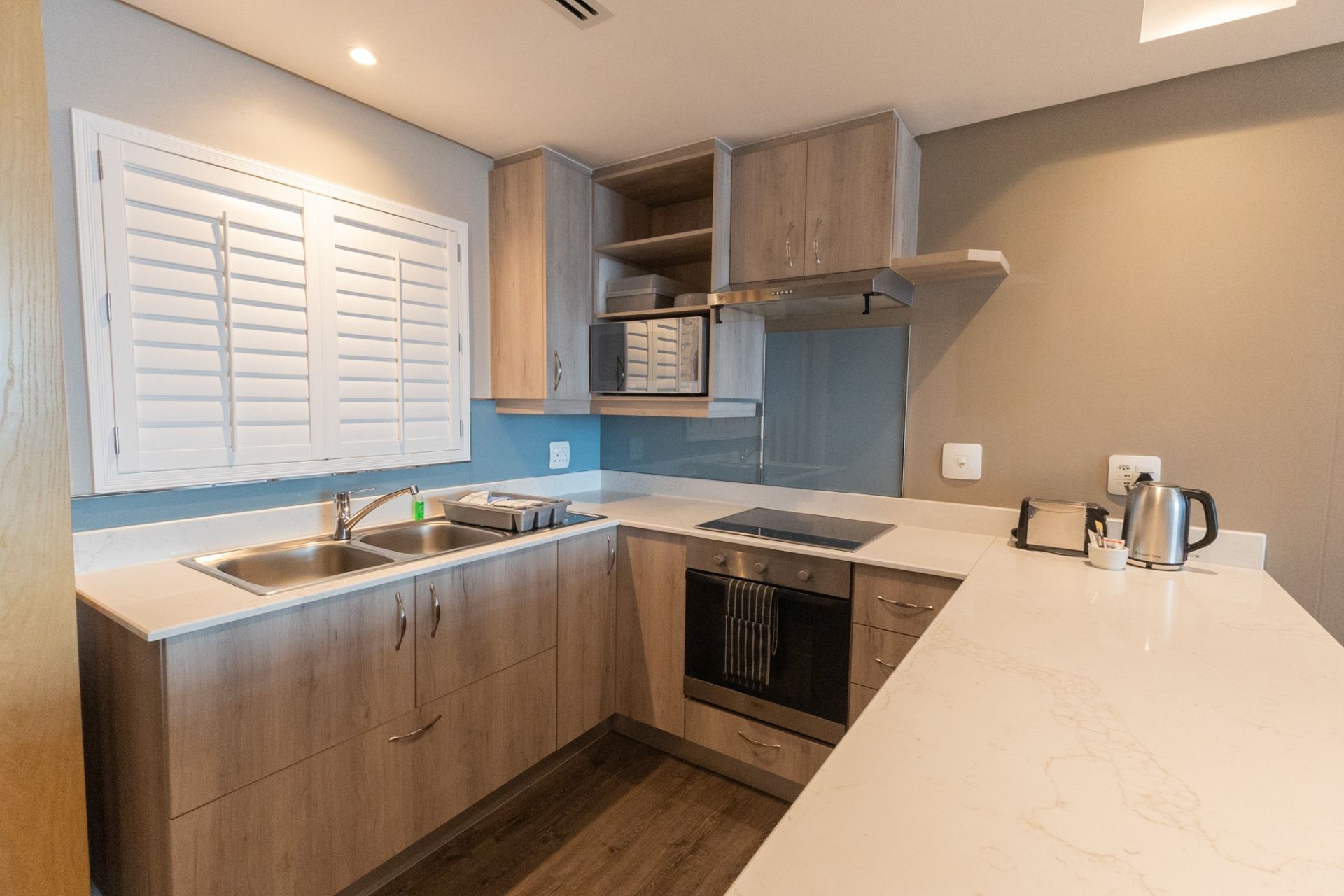 A modern kitchen with a built-in oven, a double sink, and a stainless steel kettle.