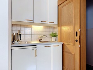A compact kitchen with white cabinets, a Bosch dishwasher, a sink, and a wooden door.