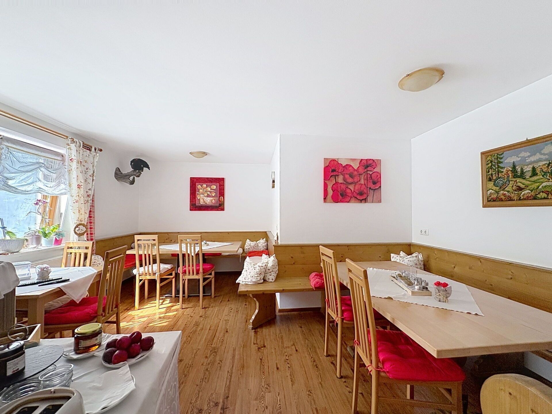 A dining area with wooden tables and chairs, a bench, and artwork on the walls.