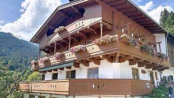 En storslagen chalet med flera våningar och balkonger som är prydda med blommor, med en imponerande bergskedja som bakgrund.
