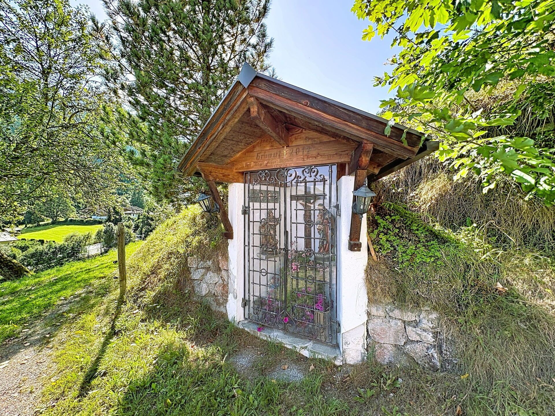 A small wooden structure with a stone base, a metal gate, and a wooden roof.