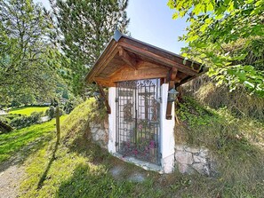 A small wooden structure with a stone base, a metal gate, and a wooden roof.