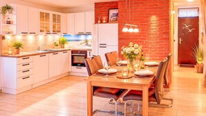 Eine moderne Küche mit weißen Schränken, einem Essbereich mit Holztisch und -stühlen sowie einer Wand mit roten Ziegelsteinen.
