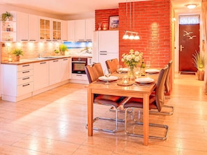 Cozinha moderna com armários brancos, área de jantar com mesa e cadeiras de madeira, e parede de tijolos vermelhos.
