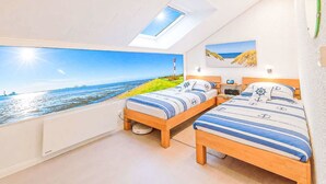Ein Schlafzimmer mit Dachfenster, zwei Betten mit Schiffsdeko, einem Strandbild und Blick auf das Meer.