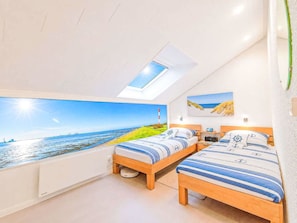 Quarto com claraboia, duas camas com roupa de cama de temática náutica, pintura de uma praia e vista para o mar.