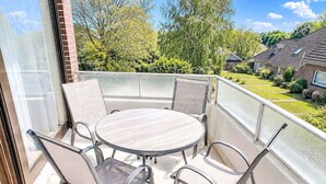 Ein Balkon mit einem runden Tisch und sechs Stühlen, umgeben von einem Metallgeländer.