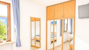Ein Schlafzimmer mit einem Bett, einem Schrank, einem Spiegel und einem Fenster mit Vorhängen.