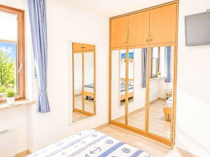 Quarto com cama, guarda-roupa, espelho e janela com cortinas.
