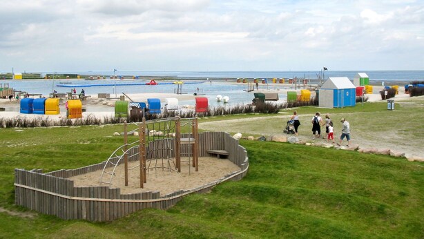 Ein Spielplatz direkt am Strand mit einer Holzspielkonstruktion und einem Sandbereich.