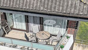 Ein Balkon mit Tisch und Stühlen, ein Fenster und eine Backsteinmauer.