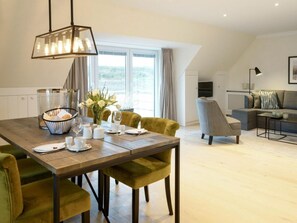 A modern dining area with a wooden table, green upholstered chairs, and a hanging light fixture. - Apartment With 1 Bedroom (Sylt)