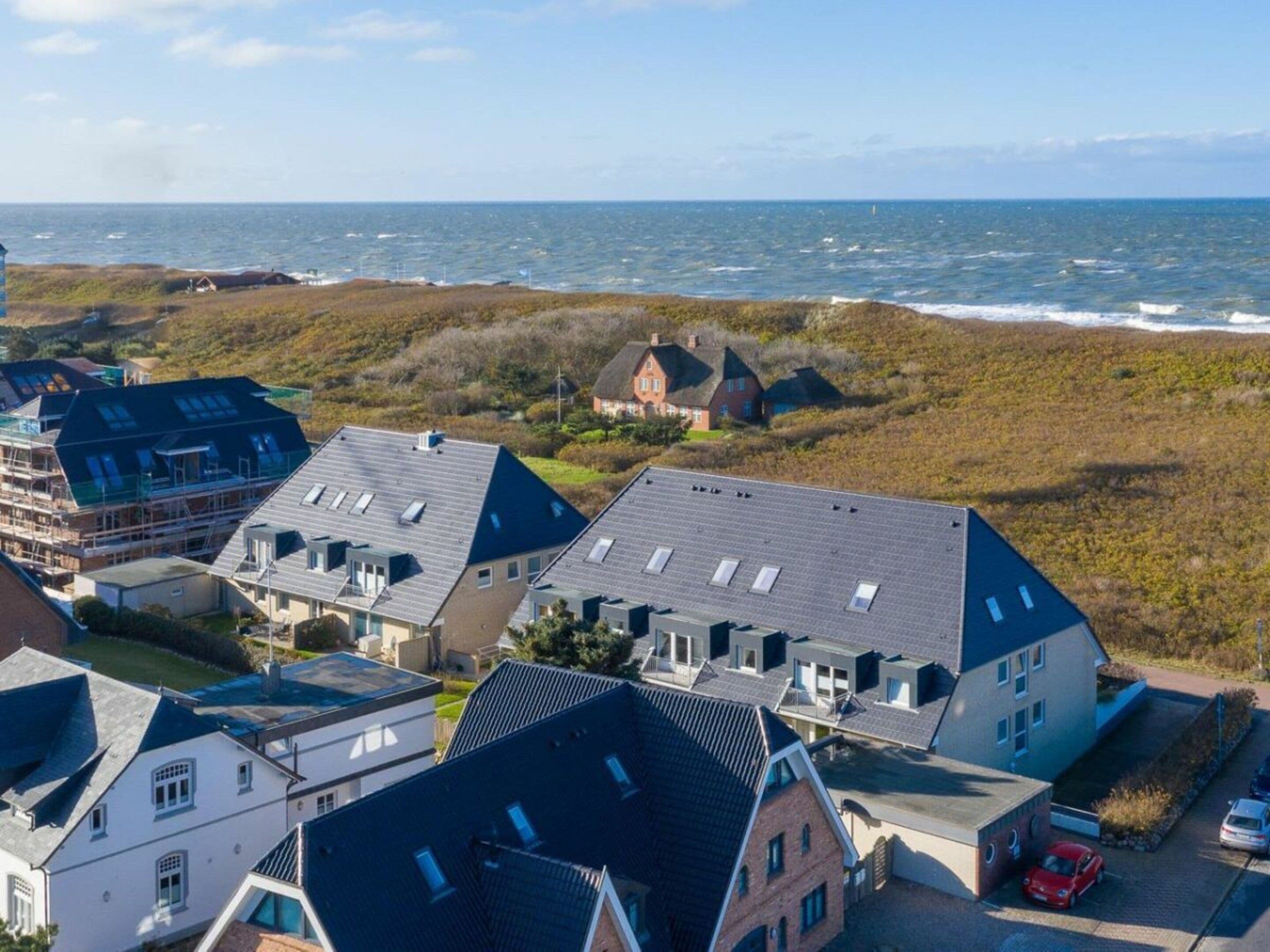 Un área residencial costera con casas, un estacionamiento y el mar al fondo.