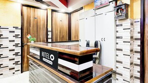 Ein Hotelrezeptionstresen mit einem Schild, das angibt, dass er firmenbetrieben wird. Es gibt Holzschränke und eine geflieste Wand mit einem geometrischen Muster.