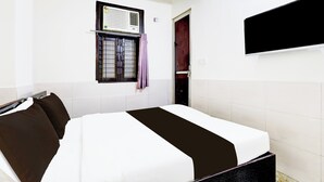 Ein Hotelzimmer mit Bett, Fenster mit Klimaanlage, Tür und flachbildschirmfernseher an der Wand.