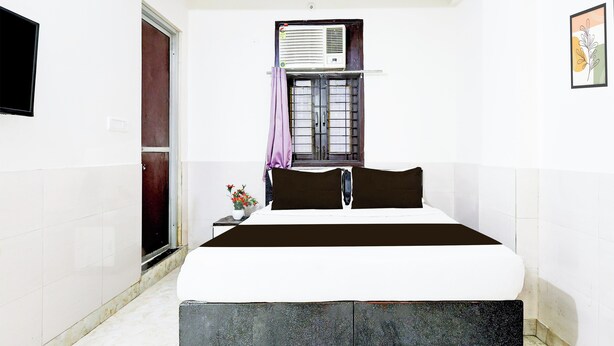Ein Schlafzimmer mit einem Bett, einem Fenster mit Vorhang, einer Wandklimaanlage und einem kleinen Tisch mit Blumen.