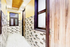 A corridor with tiled walls, a wooden door, and a window with a grid pattern. - Hotel O Fazalpur (New Delhi)