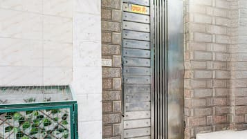Una puerta metálica con un cartel, una pared de azulejos y una verja verde de metal.