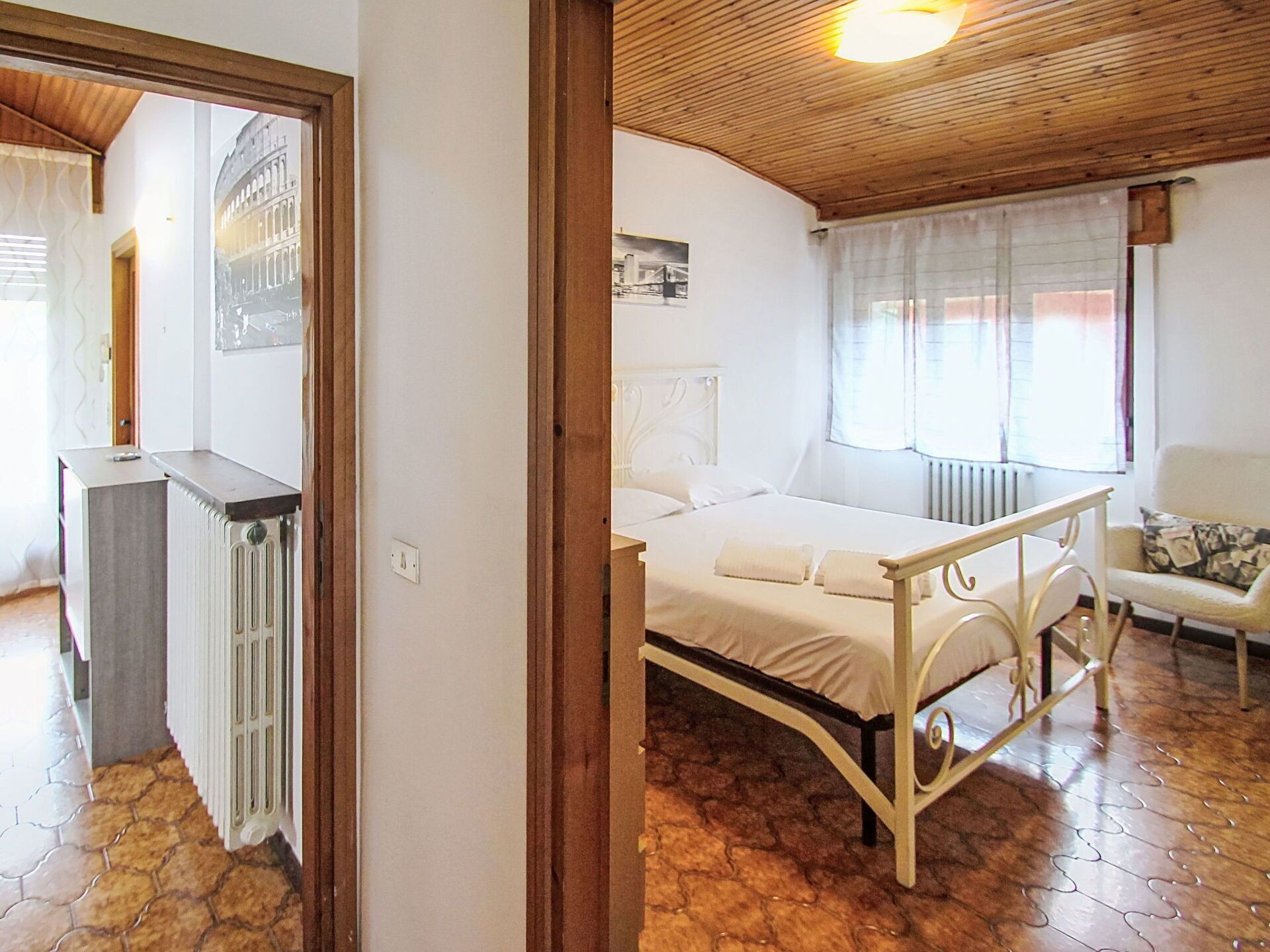 Ein Schlafzimmer mit einem Bett, einem Nachttisch, einem Heizkörper und einem Fenster mit Vorhängen.