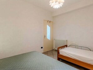 A small, sparsely furnished room with a single bed, a radiator, and a door leading to a brighter area. - Nice apartment for 5 guests with WIFI, TV, balcony and pets allowed (Garzeno)
