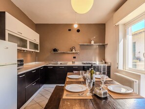 A modern kitchen with dark cabinets, a white refrigerator, and a dining area set for two with a table, plates, glasses, and a bottle. - Nice apartment for 5 guests with WIFI, TV, balcony and pets allowed (Garzeno)