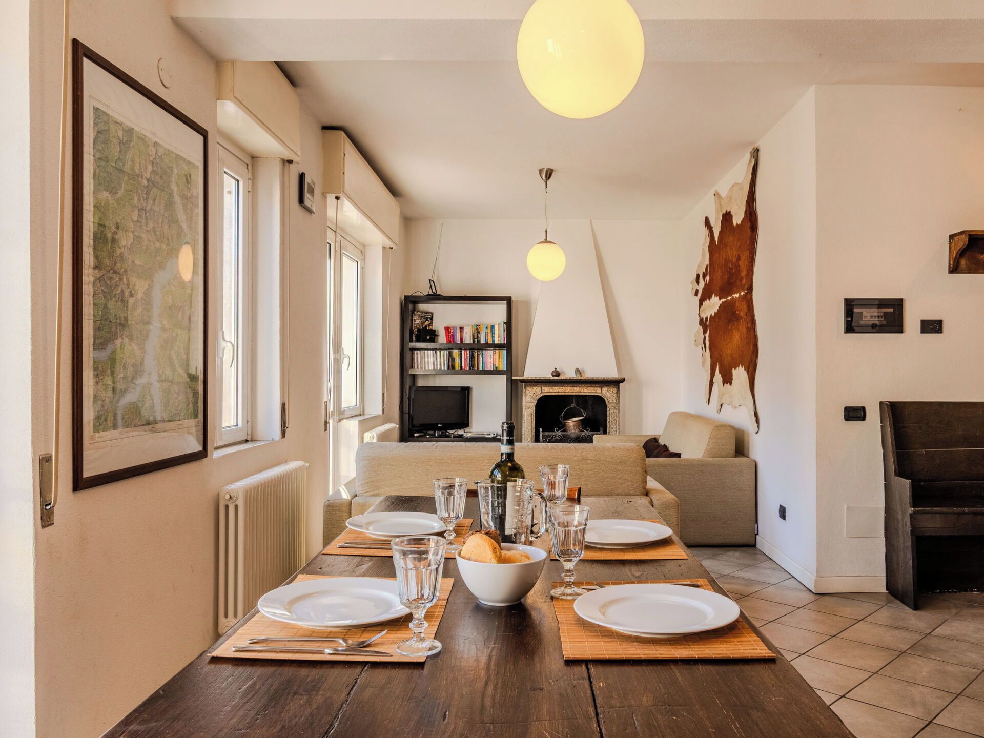 A dining area with a wooden table set for four, a fireplace, a bookshelf, and a large cowhide on the wall.