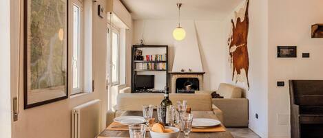 A dining area with a wooden table set for four, a fireplace, a bookshelf, and a large cowhide on the wall.