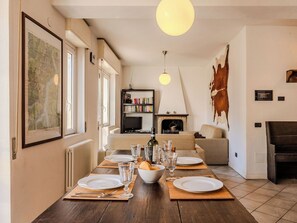 A dining area with a wooden table set for four, a fireplace, a bookshelf, and a large cowhide on the wall. - Nice apartment for 5 guests with WIFI, TV, balcony and pets allowed (Garzeno)
