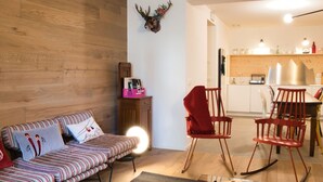 A cozy living room with a striped sofa, a red chair, a wooden wall, and a kitchen area in the background. - Lovely apartment for 6 people with WIFI and TV (Bormio)