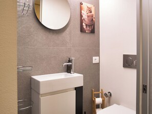 Une salle de bain moderne avec un lavabo blanc, un miroir rond et un porte-rouleau de papier toilette.
