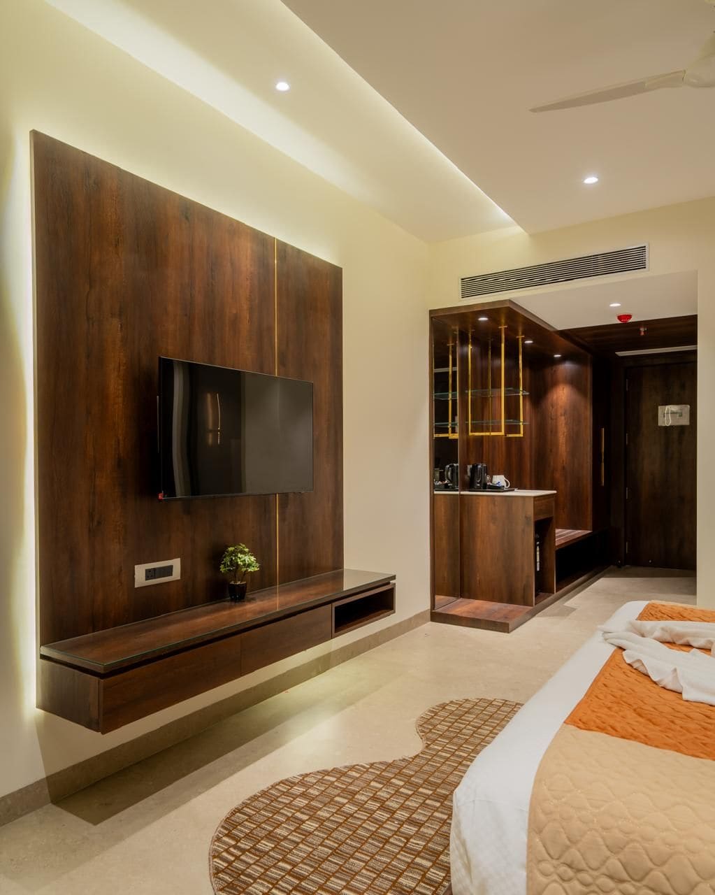 A modern bedroom with a flat-screen TV, built-in shelving, a bedside table, and a patterned rug.