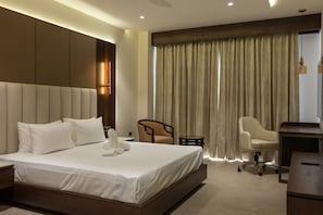 Quarto de hotel com uma cama grande, escrivaninha, cadeira e janela com cortinas.