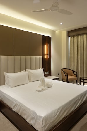 Quarto de hotel com uma cama grande, uma cadeira, uma mesinha e um ventilador de teto.