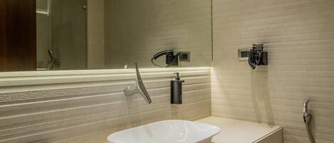 A modern bathroom with a large mirror, a white sink, and a wooden vanity.