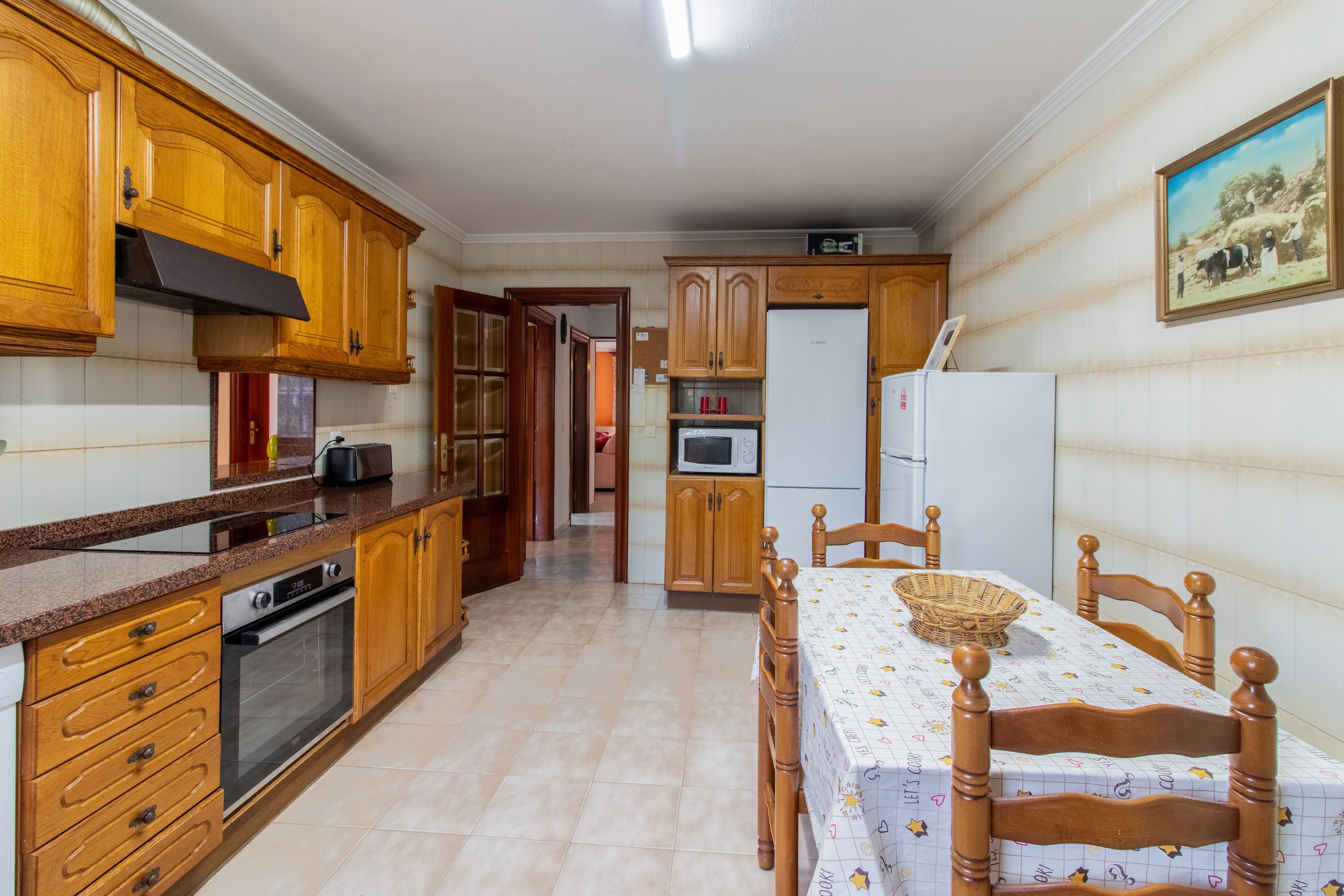 Una cocina con armarios de madera, una mesa de comedor con sillas y un refrigerador.