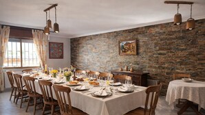 Une salle à manger avec un mur en briques, des chaises en bois, une longue table dressée pour le repas et des luminaires suspendus.