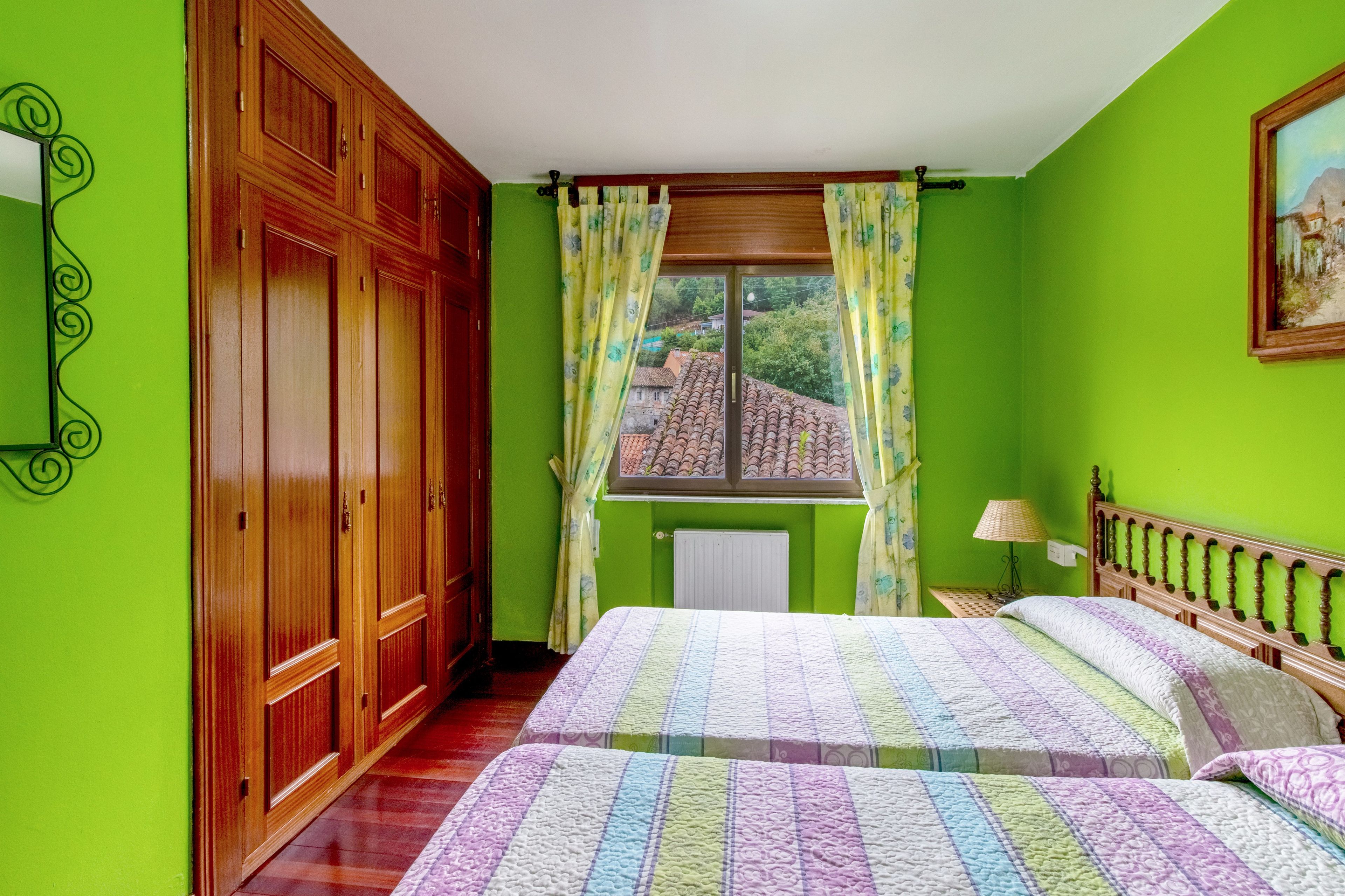 A bedroom with two beds, a window with curtains, a radiator, and a wooden wardrobe.