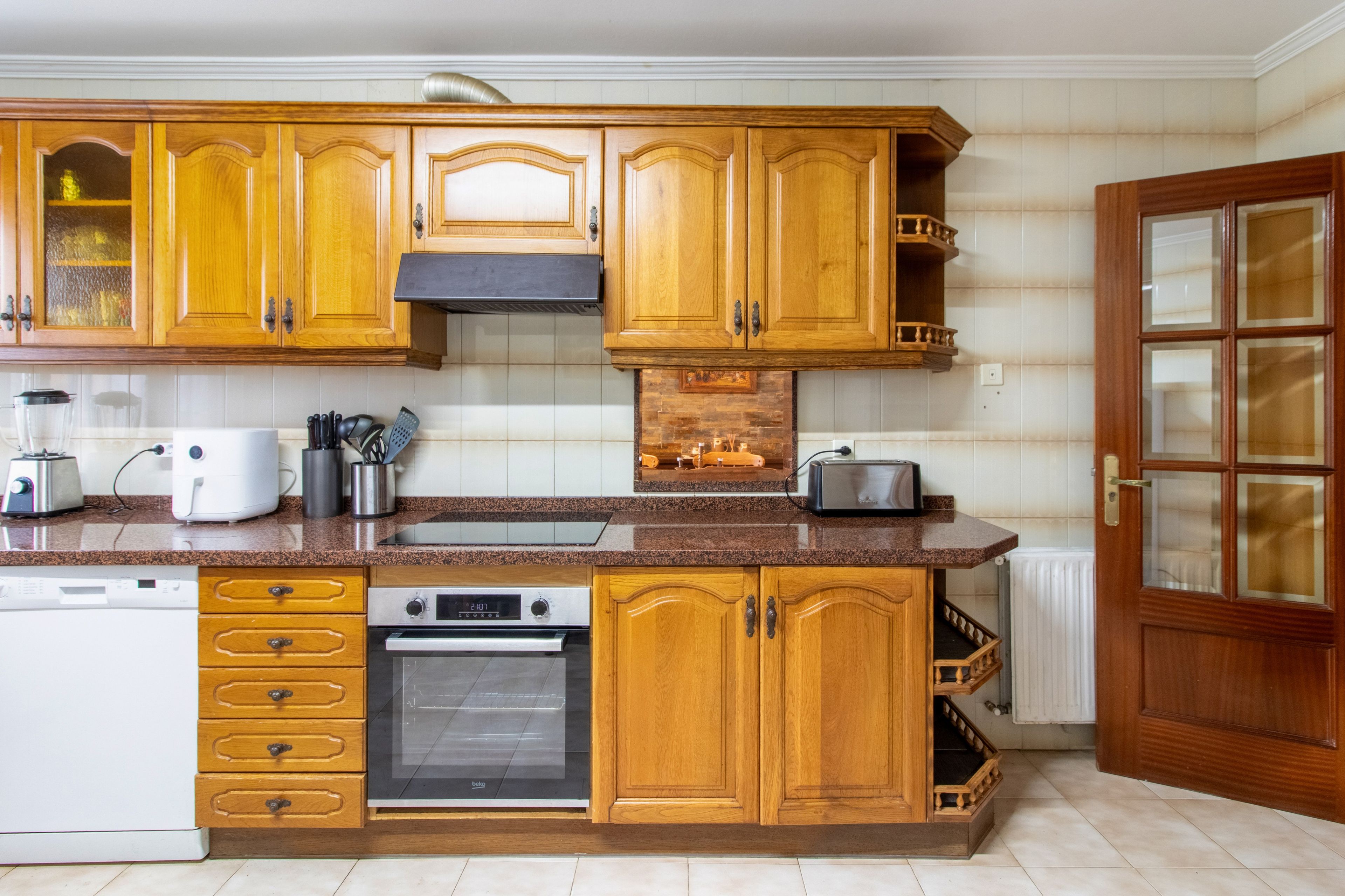 A kitchen with wooden cabinets, a built-in oven, a toaster, and a dishwasher.