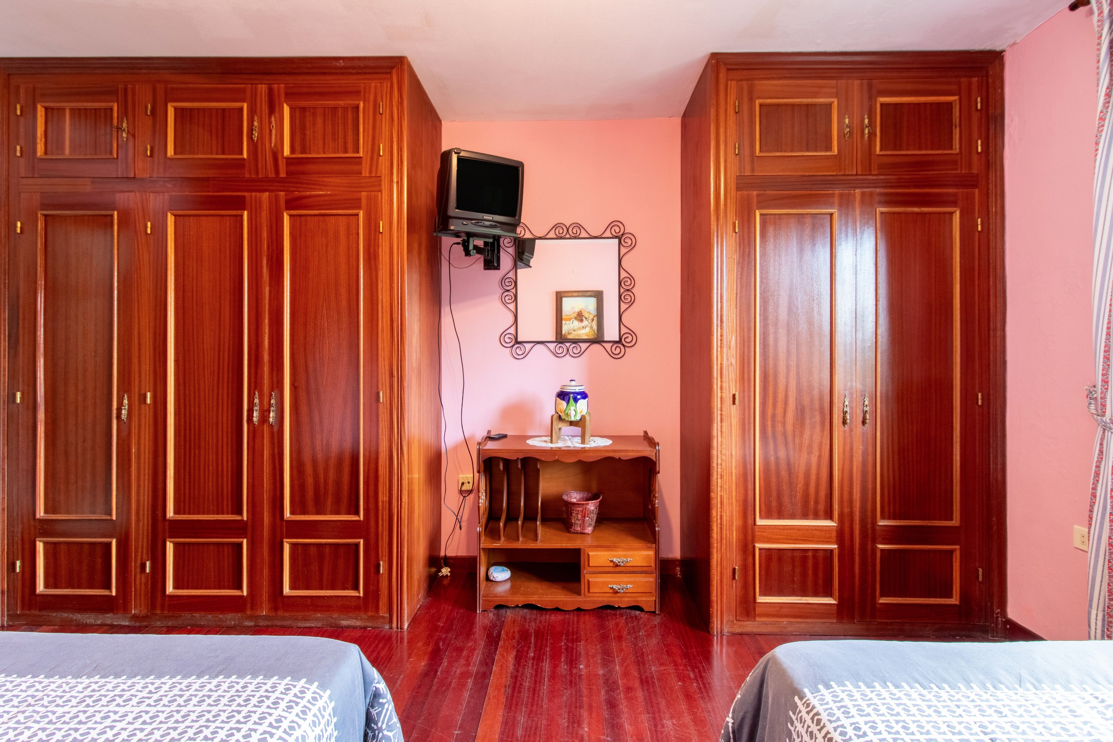 A room with two wooden wardrobes, a television mounted on the wall, and a small table with a vase and a picture frame.