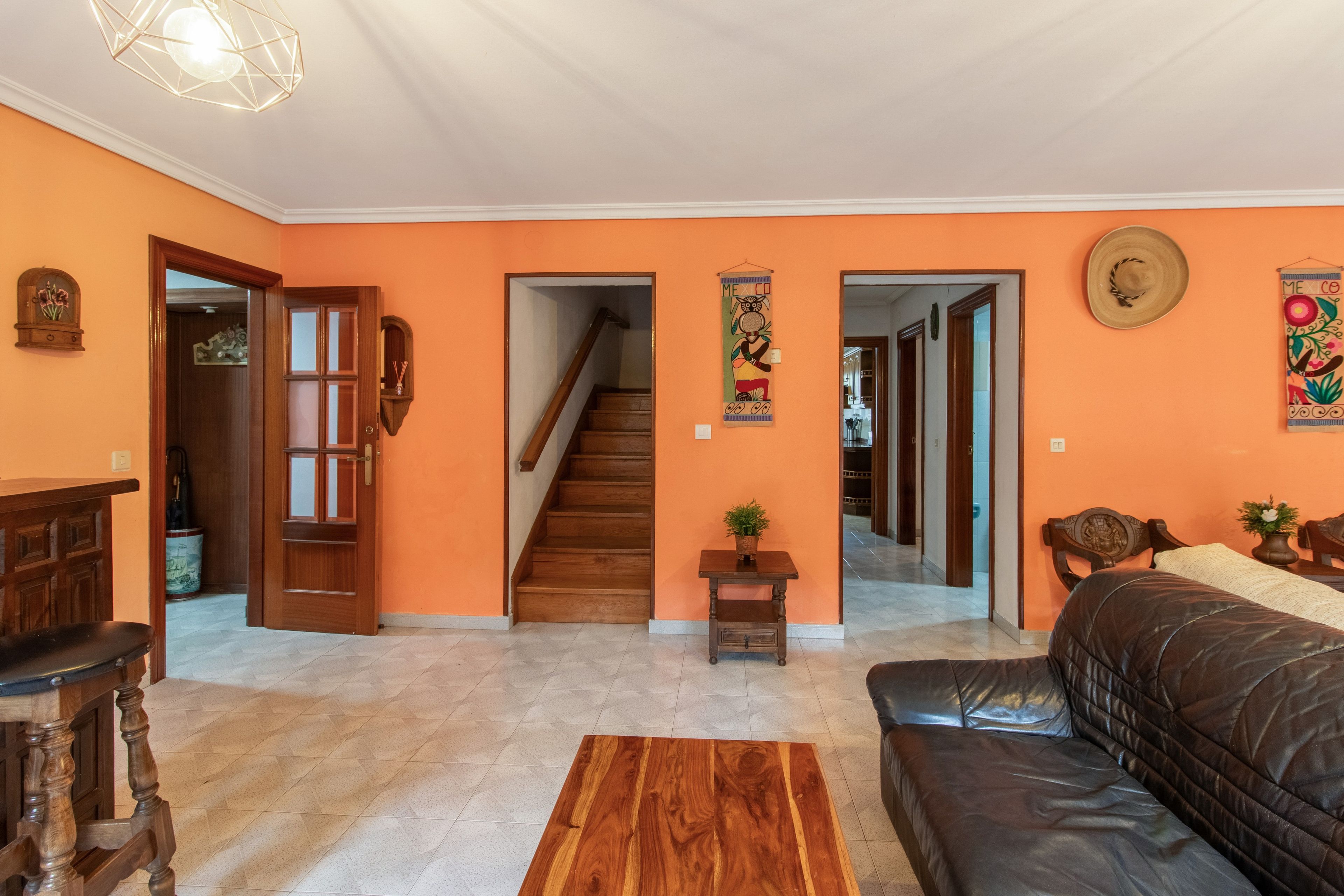 Una sala de estar con piso de madera, un sofá de cuero negro, una mesa de centro de madera y una escalera que conduce a otra habitación.