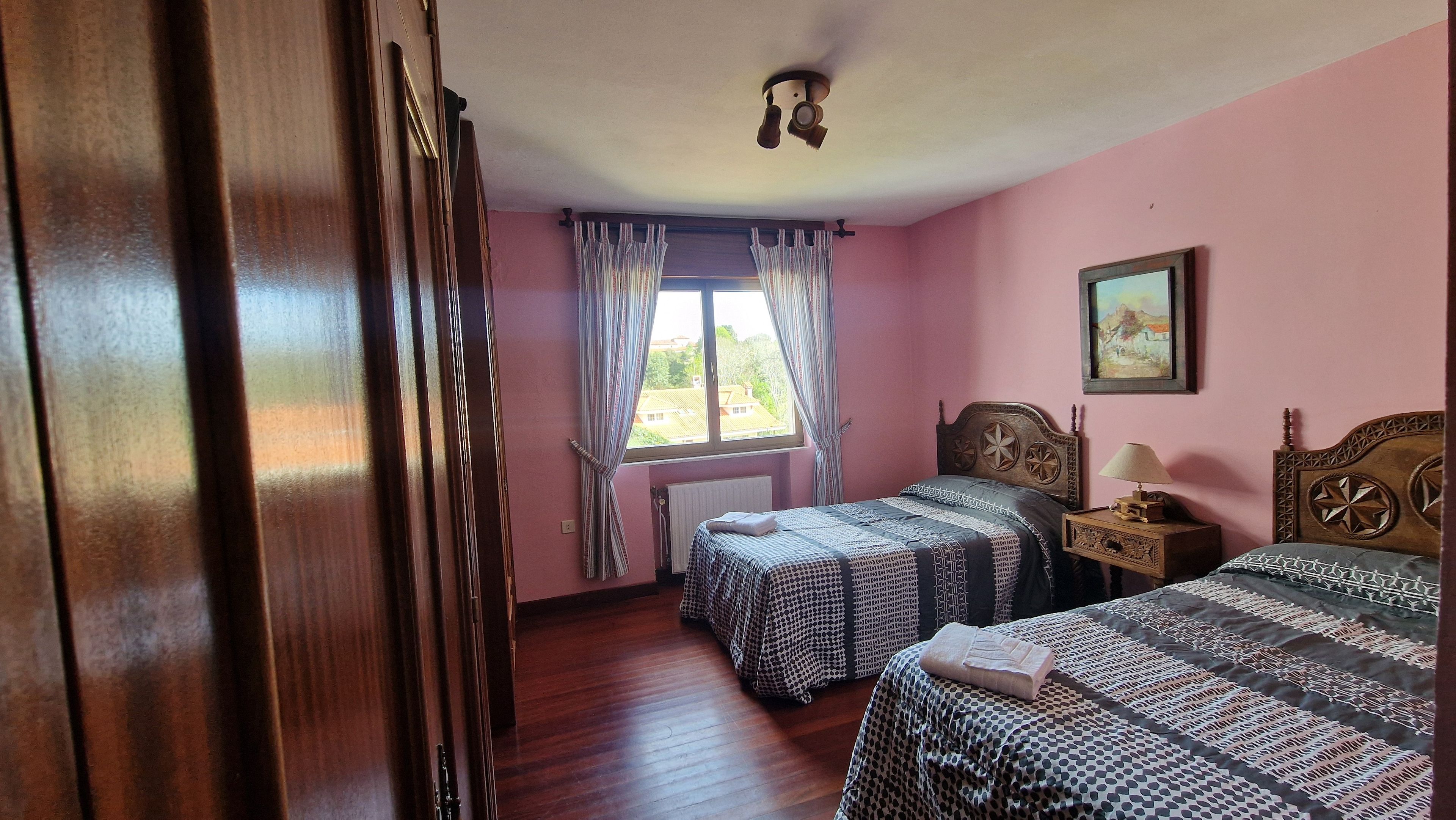 Quarto com duas camas, janela com cortinas, radiador e um quadro na parede.
