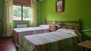 Une chambre avec deux lits, une fenêtre avec des rideaux, une table de chevet avec une lampe et un tableau au mur.