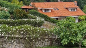 Un bâtiment avec un toit recouvert de tuiles rouges, entouré de verdure et délimité par un mur de pierre.