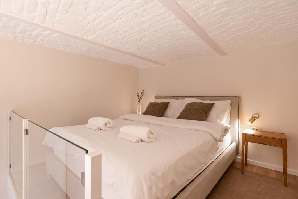 A bedroom with a bed, a bedside table, a lamp, and a glass door leading to a balcony.