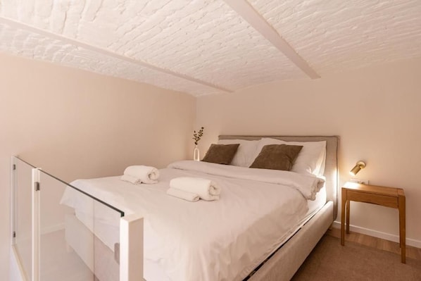 A bedroom with a bed, a bedside table, a lamp, and a glass door leading to a balcony.