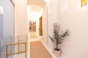 A hallway with a glass railing, a potted plant, and a carpeted floor.