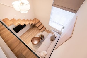 A modern interior with a staircase leading to a living area, a sofa, and a round wooden table.
