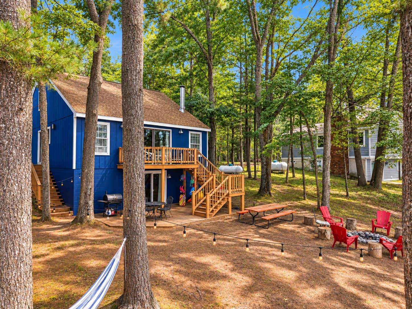A blue cabin with a wooden deck, outdoor seating, and a hammock.