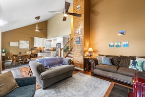 A spacious living area with a sofa, a dining table, and a kitchen in the background. - Lakefront on Lake Wequas | Private Beach, Dock + Kayaks (Gaylord)